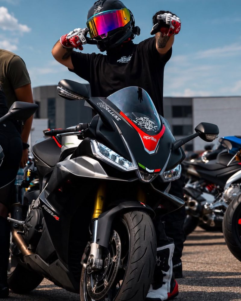 Luke in his helmet and riding gloves, posing behind his Aprilia RSV4
